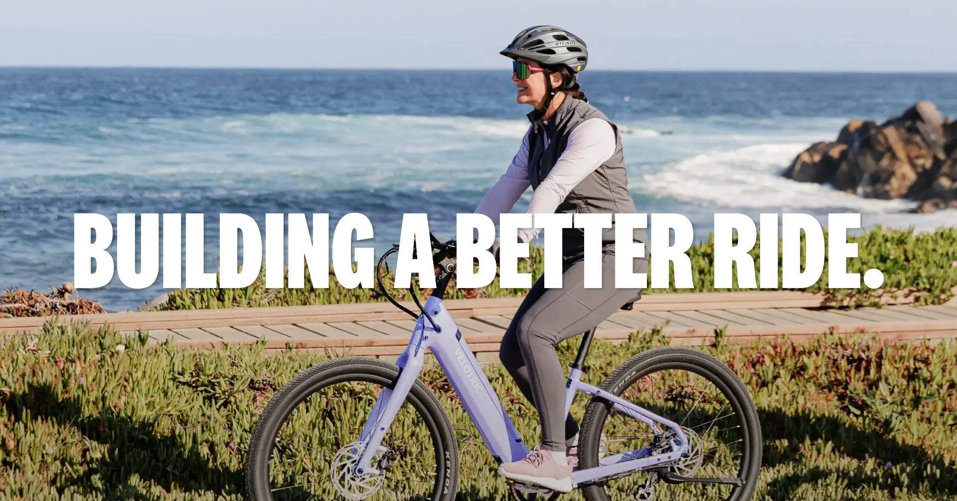 Rider smiling on a lavender Velotric e-bike along a coastal boardwalk — Building a better ride