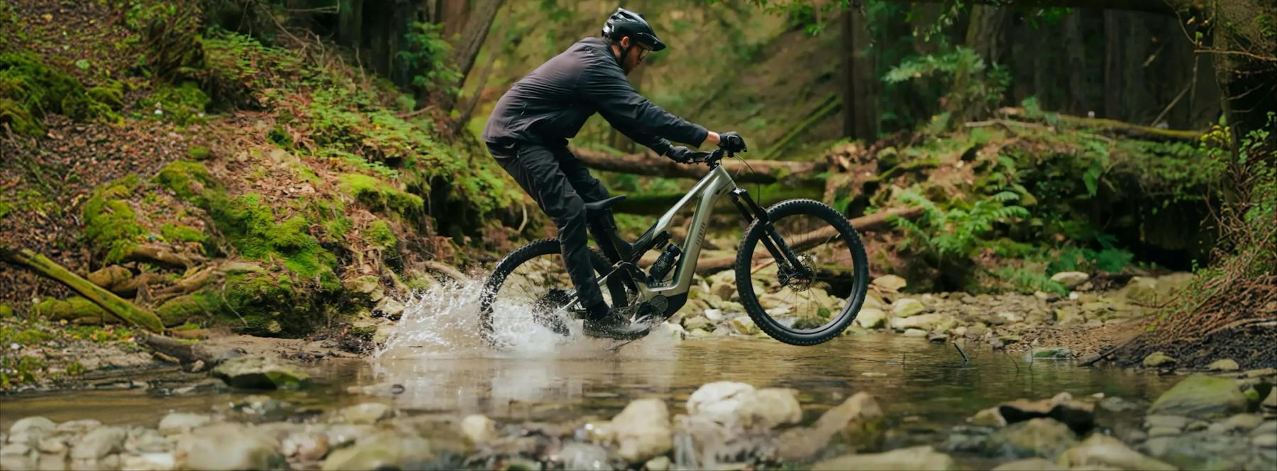 Aventon rider crossing a forest stream on an e-mountain bike